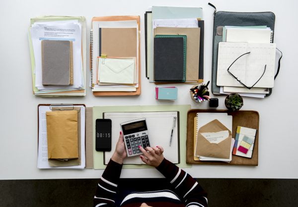 Hands Working on Office Desk with Notebooks and Stationery on White Table